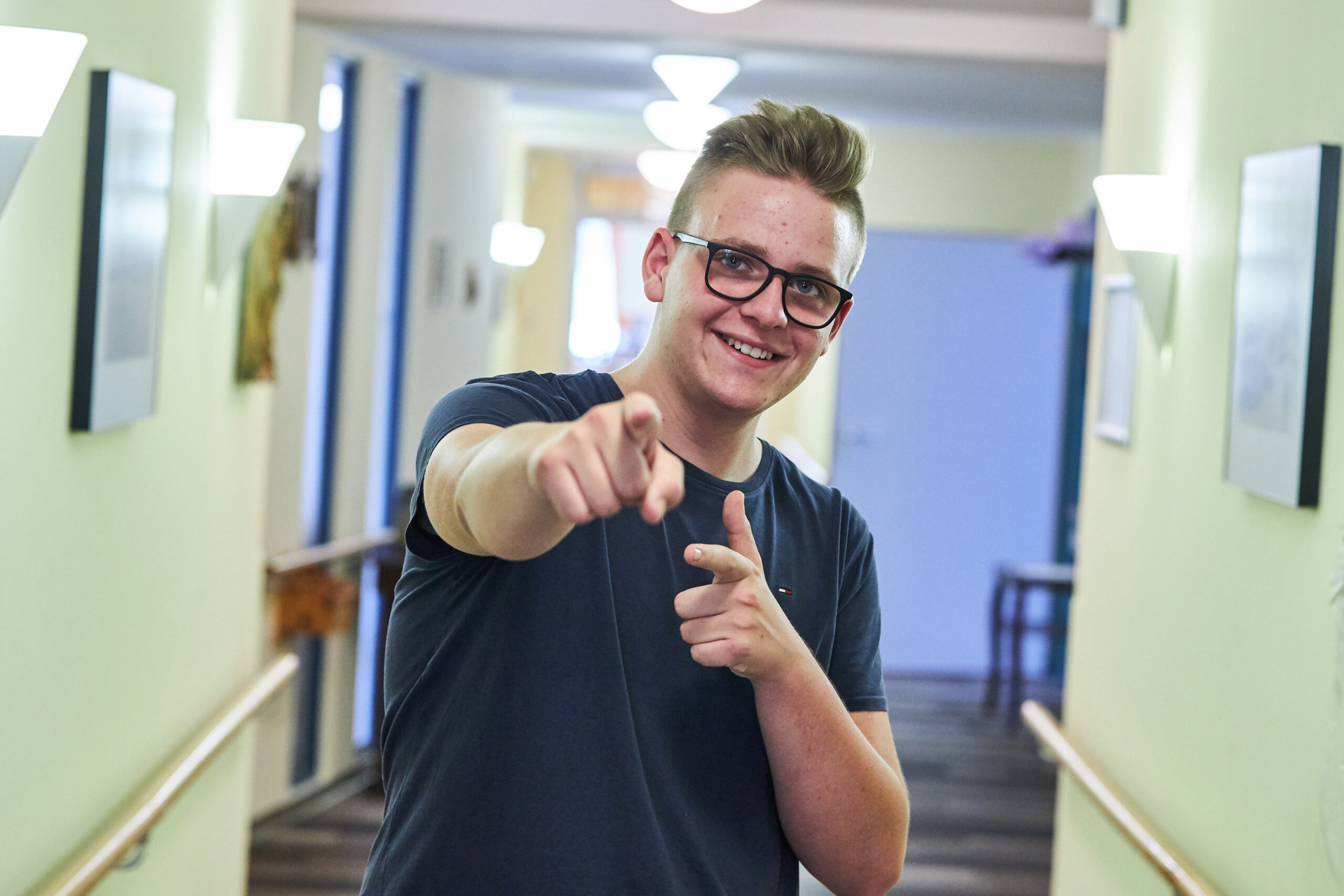 Junger Mann mit Brille, deutet zur Kamera