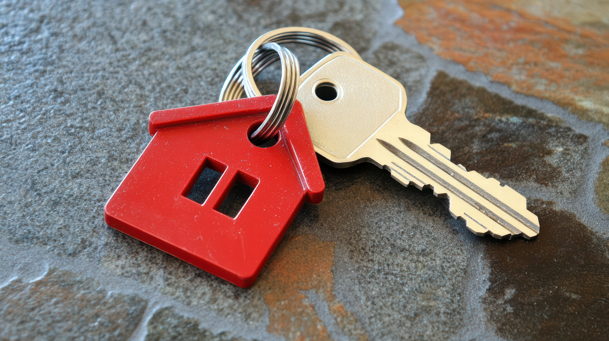 key with house shaped keychain resting on stone surface symbolizes home ownership and security